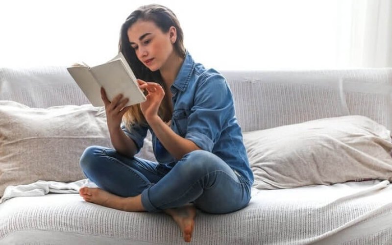 mulher sentada no sofá lendo livro