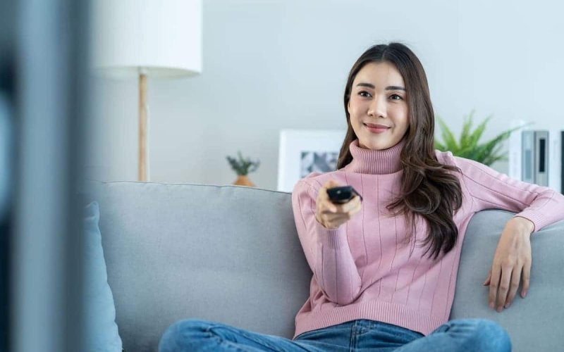 mulher sentada no sofá confortávelmente utilizando o controle da televisão
