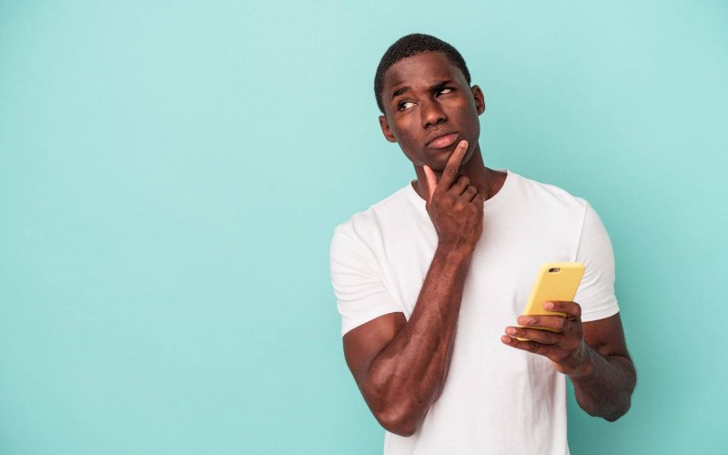 Homem pensando com o celular na mão